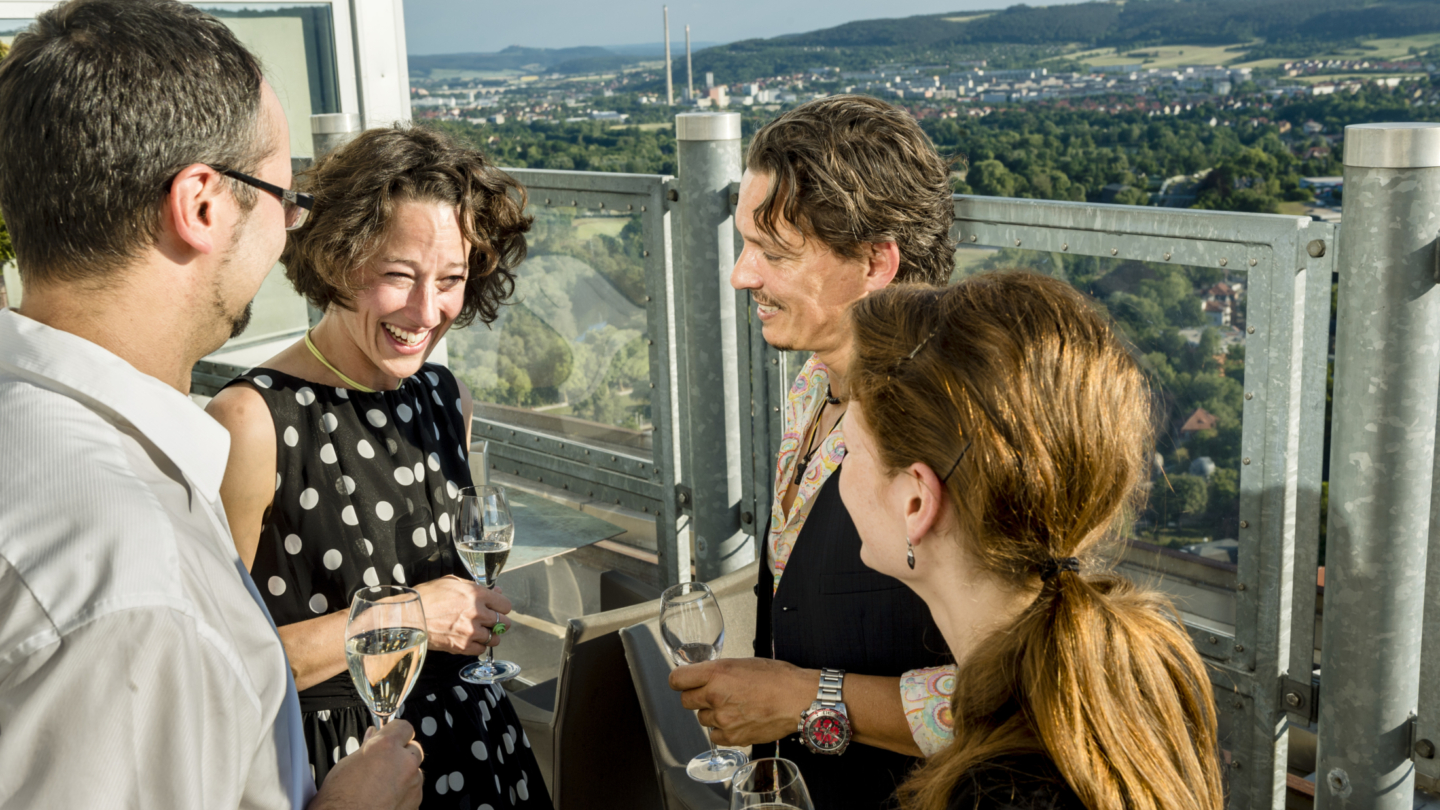 Personen auf der Ausichtsplatform des JenTower trinken ein Glas Sekt mit der Stadt im Hintergrund © JenaKultur, Foto: Andreas Hub