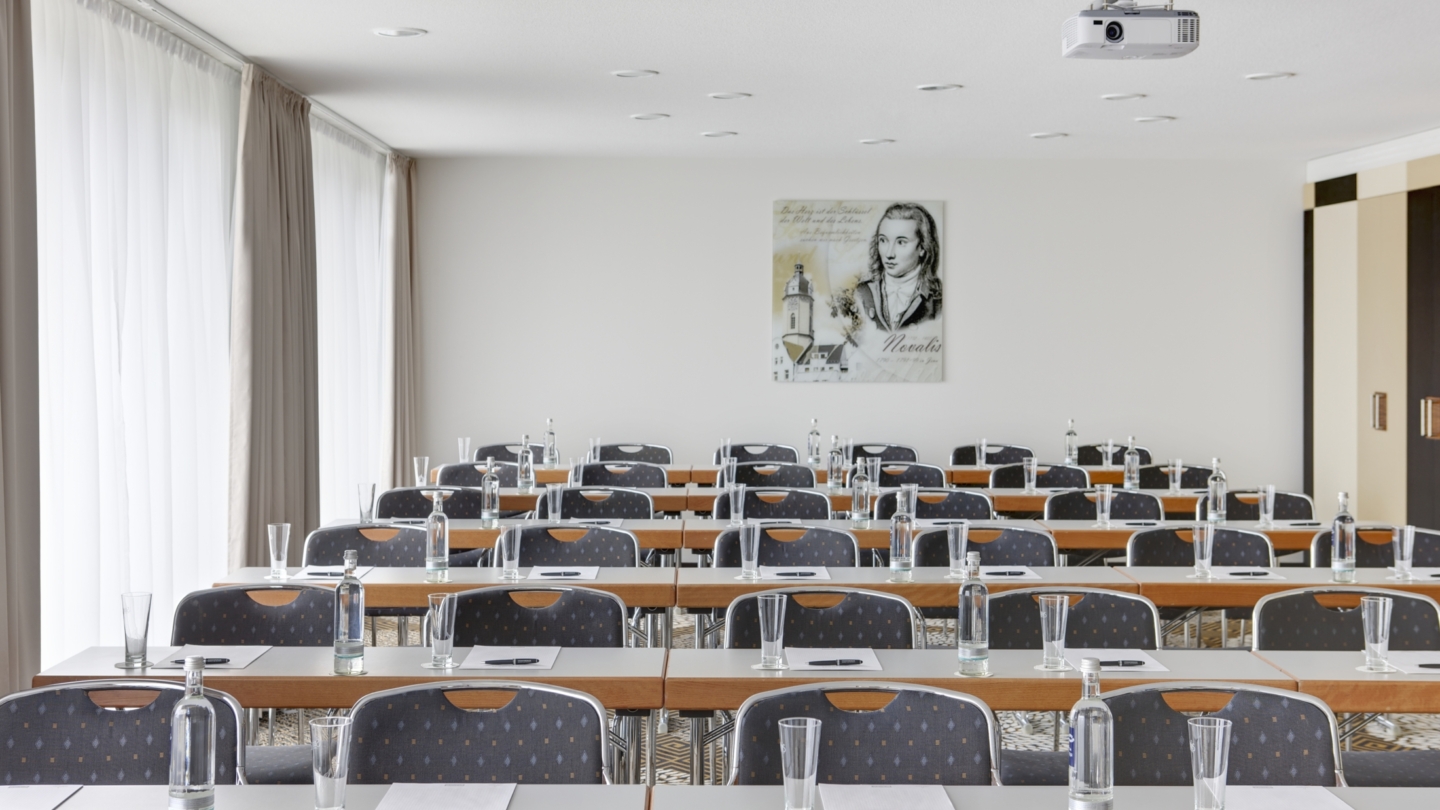 Steigenberger Esplanade Hotel Jena, Salon Novalis © Deutsche Hospitality, Foto: unbekannt Raum in Parlament-Bestuhlung mit Schreibutensilien, Getränken und einem Portrait von Novalis im Hintergrund © Deutsche Hospitality, Foto: unbekannt